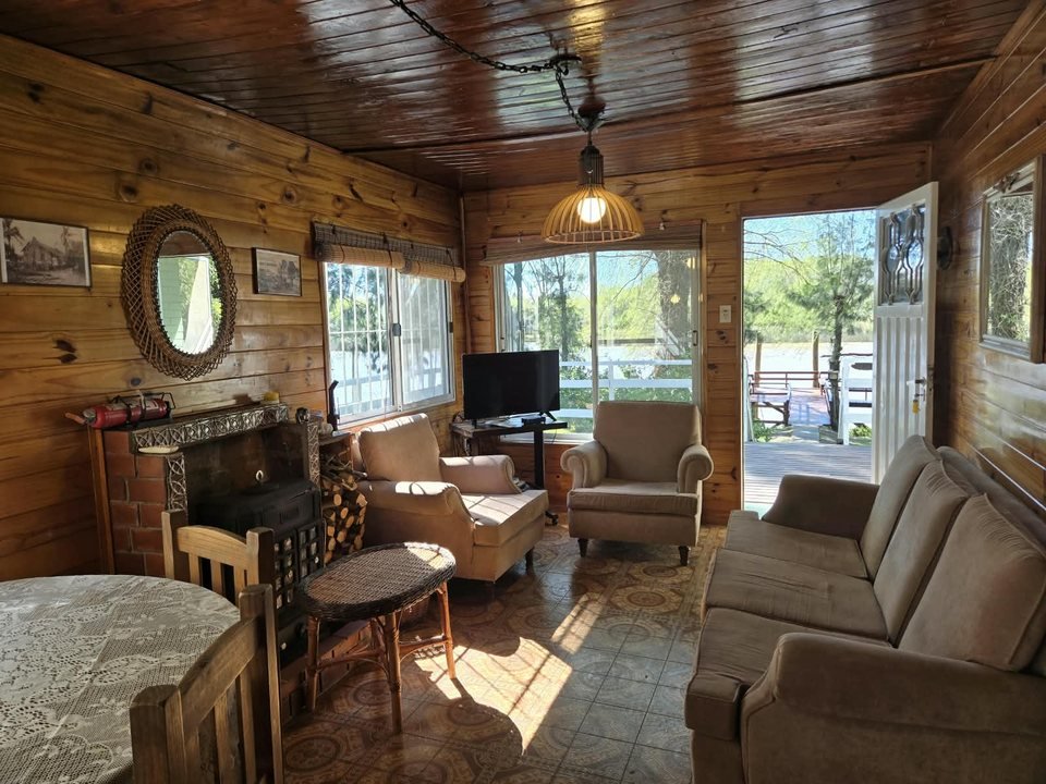 Living comedor de madera con sillones, hogar a leña y vista al río